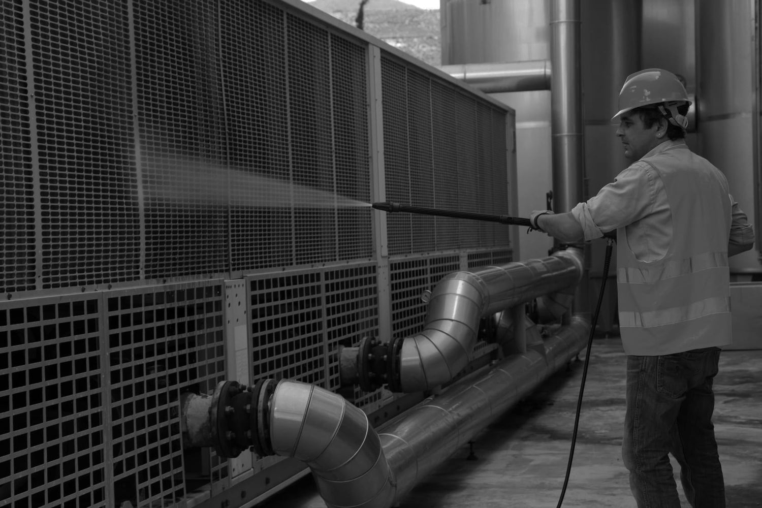 black and white image of a man using a power washer in an industrial space